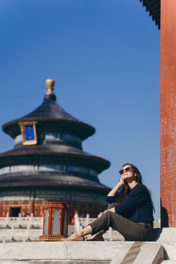 mujer sentada bajo el sol frente a un templo chino
